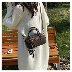 Detail of dark brown pillow bag with gold hardware and charms in an autumn park setting