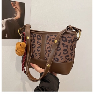 Detail of leopard print bucket bag with plush bear charm and striped textile strap