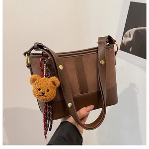 Detail of brown patchwork shoulder bag with bear charm and decorative gold rivets