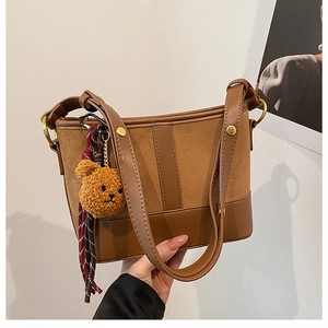 Detail of a brown bucket bag featuring faux suede panels and a plush bear charm