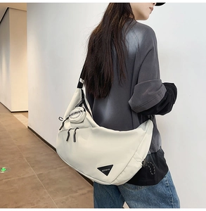 Detail of cream croissant bag with black KIEIMAN brand logo and mini pouch pendant