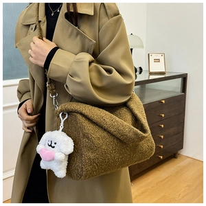 Detail of a brown plush shoulder bag with a cute white puppy charm and silver buckle