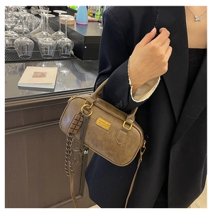 Detailed close-up of dark brown Boston bag with gold metal plate and chocolate charm