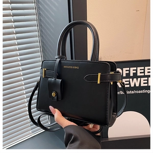 Détail du petit sac carré en cuir noir avec logo doré et sangle à boucle métallique
