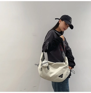 Detail view of cream dumpling crossbody bag with round pendant and logo patch