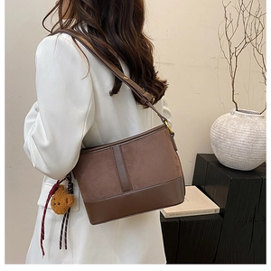 Detail of dark brown bucket bag with plush bear charm and adjustable shoulder strap