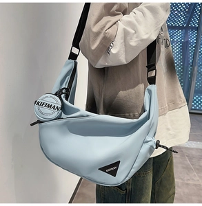 Detail of light blue crescent bag with black adjustable strap and brand logo