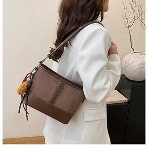 Close-up of brown patchwork bucket bag featuring suede texture and plush ball charm