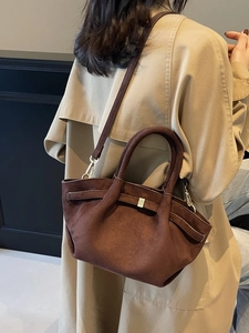 Braune matte Wildleder-Einkaufstasche mit Metallschnallen an einem Model im Trenchcoat