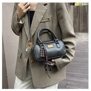 Detail of black Boston bag featuring golden logo plate and cute cartoon cat charms
