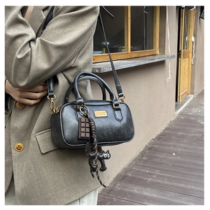 Macro detail of black vintage leather boston bag with gold plaque and cat charm accessories