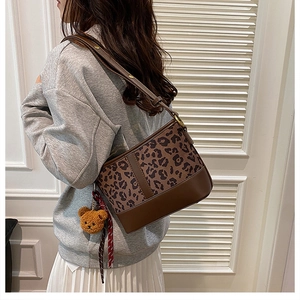 Close-up of leopard print bucket bag with plush bear charm and plaid ribbon detail