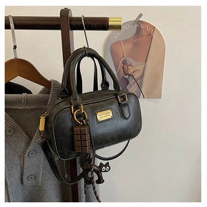 Detail of black Boston bag with gold nameplate, cat charm and chocolate pendant decoration