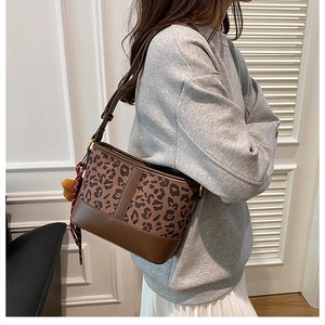 Detailed leopard print hobo bag with a red striped scarf charm and yellow fur ball accessory