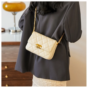 Detail of quilted leather texture and golden metal chain strap on cream crossbody bag