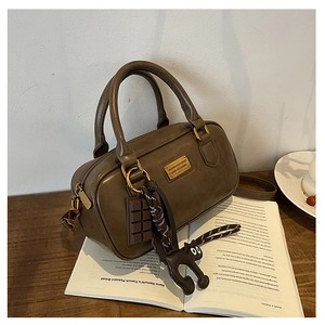Close-up of brown leather pillow bag with gold logo plaque and black cat keychain