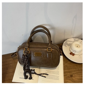 Close-up of retro brown PU leather boston bag with gold nameplate and cute cat charm