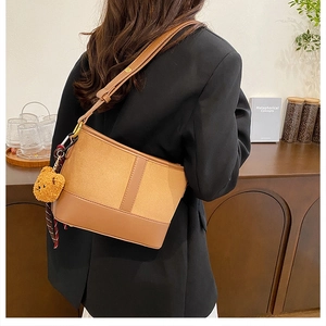 Detail of a brown leather shoulder bag with a plush bear charm and plaid ribbon accessory