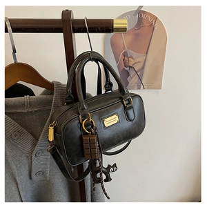 Detail of black Boston bag with gold zipper, chocolate charm and cute cat pendant