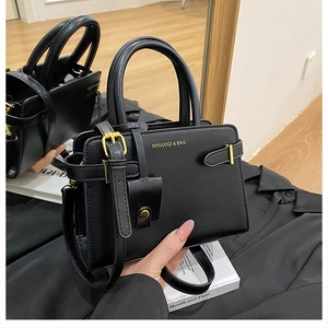 Détail du sac en cuir noir avec logo doré et boucle de réglage de la bandoulière amovible