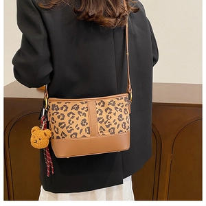 Detail of leopard print bucket bag featuring a cute plush bear charm on the strap