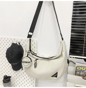 Detail of off-white nylon crescent bag with wide black strap and round coin pouch charm