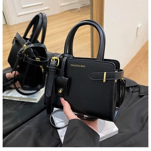 Détail d'un sac carré en cuir noir avec lettrage doré et mini pochette amovible chic