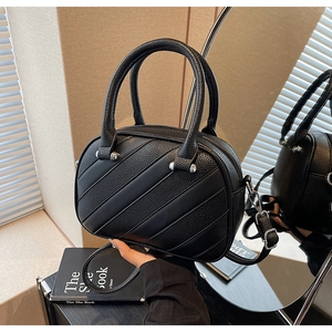Dettaglio della borsa in pelle nera con venature, cuciture diagonali e borchie in metallo