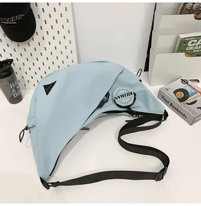Detail of light blue crescent bag with adjustable black strap and brand tag on zipper