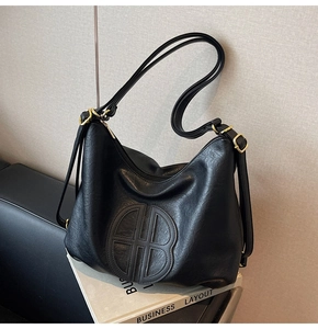 Detail of black textured faux leather tote bag with embossed circular logo and gold hardware