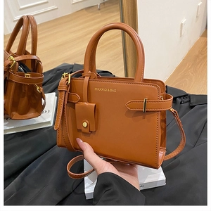 Détail d'un sac à main en cuir mat caramel avec logo doré et petit accessoire assorti