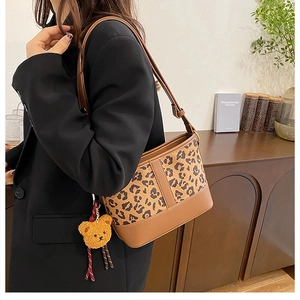 Detail view of leopard print bucket bag with brown leather trim and plush bear charm