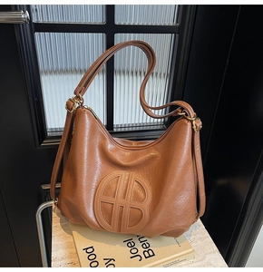 Detail of a brown leather hobo bag featuring a circular cutout logo and gold hardware