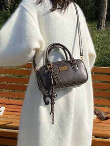 Deep brown Boston bag with cat pendant and chocolate charm shown on a park bench