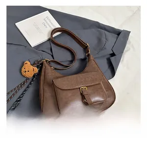 Détail du sac demi-lune marron rétro avec boucle dorée et breloque ours sur blazer gris