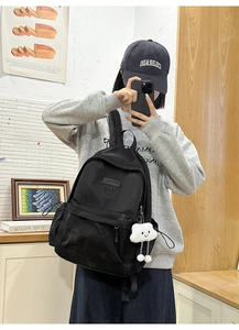 Detail of black casual backpack with subtle smiley pattern and white cloud plush pendant