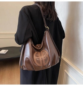 Detail of soft dark brown leather tote bag with round logo and gold metal buckle