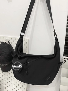 Minimalist black crescent crossbody bag with adjustable strap on white pegboard