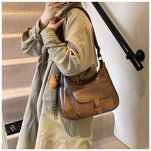Sac hobo marron en cuir huilé avec breloque d'ours porté sur un mannequin en trench