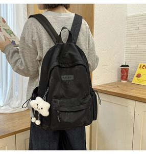Detail of black backpack with smiley face patterns and a white cloud plush charm
