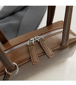 Detail of vintage brown leather handbag featuring dual silver zippers and precise stitching