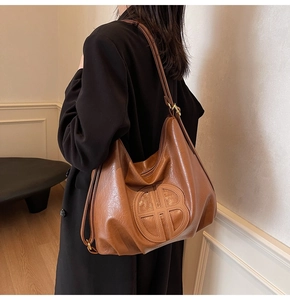 Close-up of brown soft leather tote bag featuring a circular embossed logo and slim strap