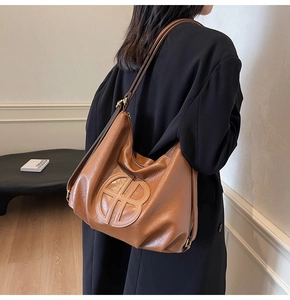 Detailed close-up of textured brown leather tote bag with embossed circular logo