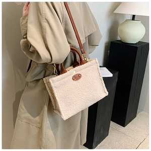 Plush off-white tote bag with brown leather straps shown on a model in a trench coat