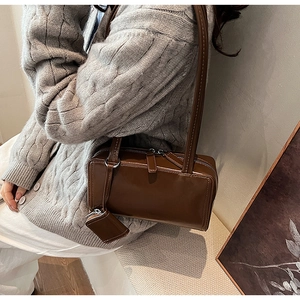 Detail of vintage brown underarm bag with mini pouch charm worn with grey knitwear
