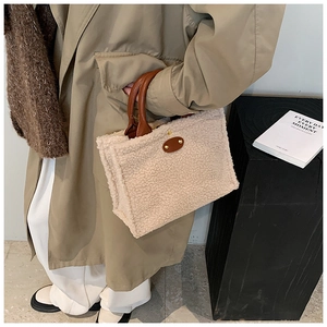 Detail view of beige plush fleece shoulder bag with brown leather handles and gold studs