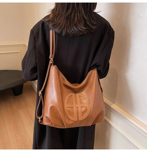 Caramel brown soft leather hobo bag with embossed logo worn with a black wool coat