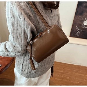 Detail of dark brown polished leather shoulder bag styled with grey knit sweater