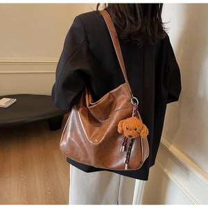 Detail of vintage brown tote bag with cute teddy bear plush charm in home setting