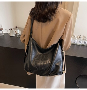 Detail of black pebbled leather hobo bag with embossed GB logo on a female model